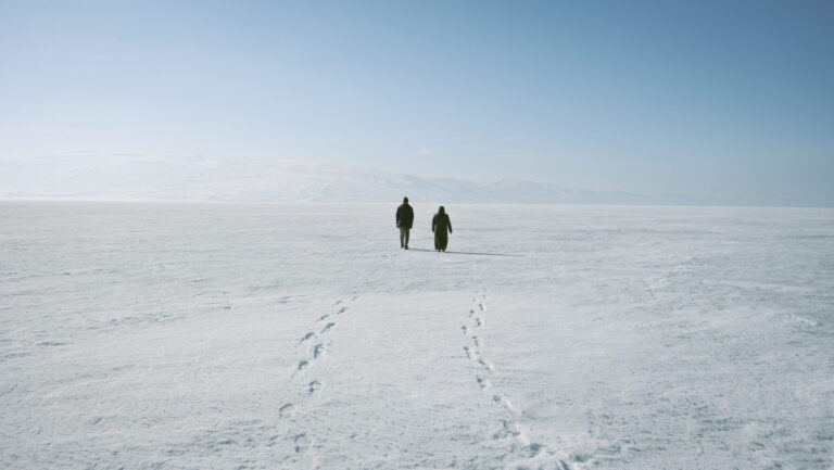 A back view of two persons walking on a snow covered ground