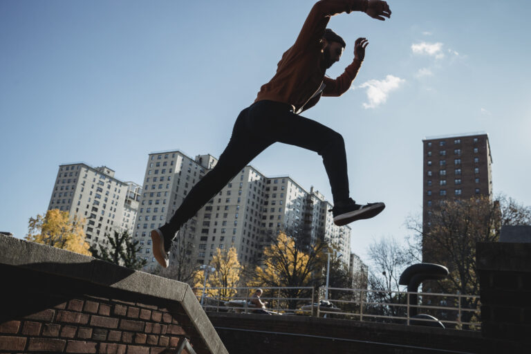 Fit man jumping from brick parapet in urban city