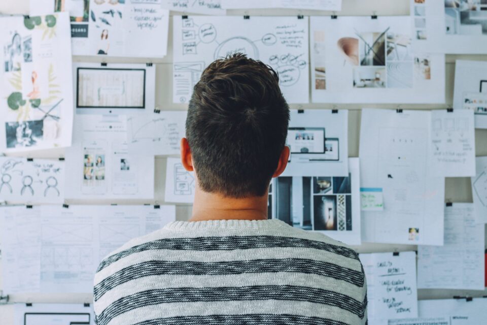 Man wearing black and white stripe shirt looking at white printer papers on the wall