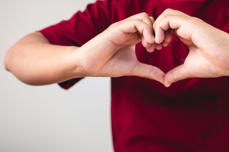 Person shows hands sign of love near the chest. The man with red shirt in medium close up shot. Valentine's concept. Copy space for messages, words and texts.