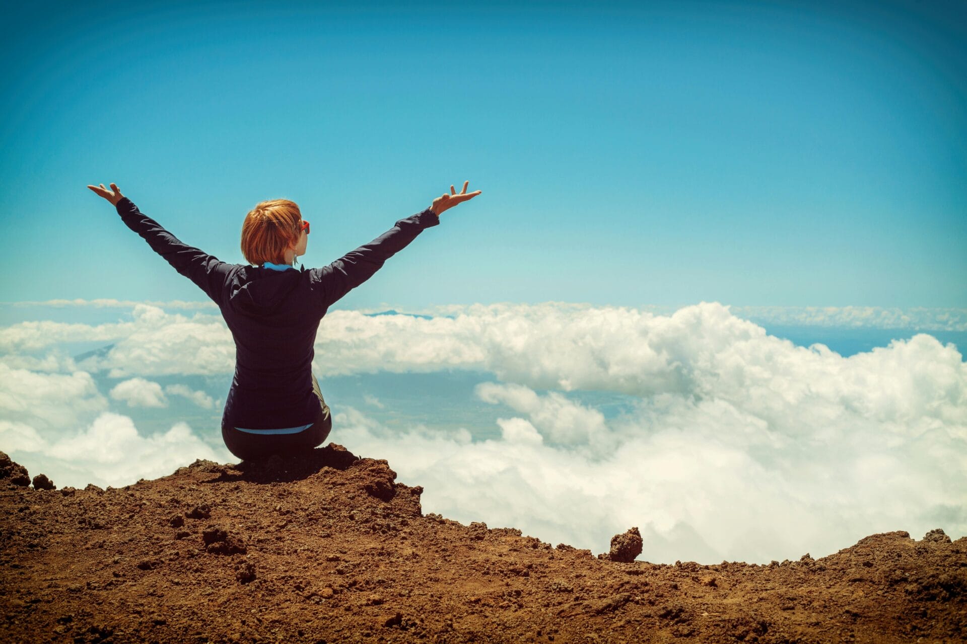 Person sitting on cliff raising up both hands