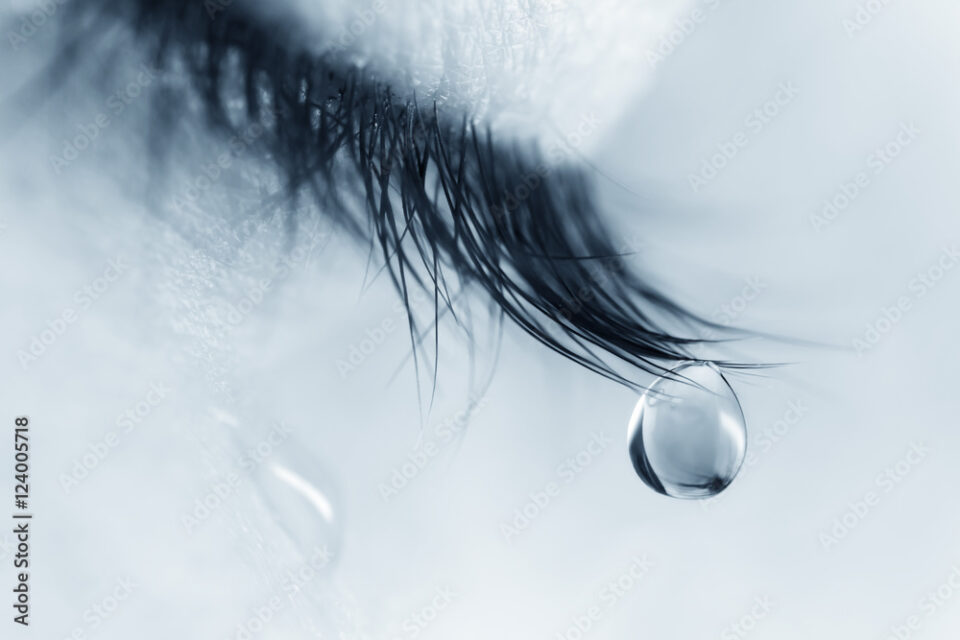 Sad woman concept - closed eyelid closeup with a teardrop on eyelashes.  A tear on eyelashes macro close-up. A tear runs down his cheek. Tinted blue.