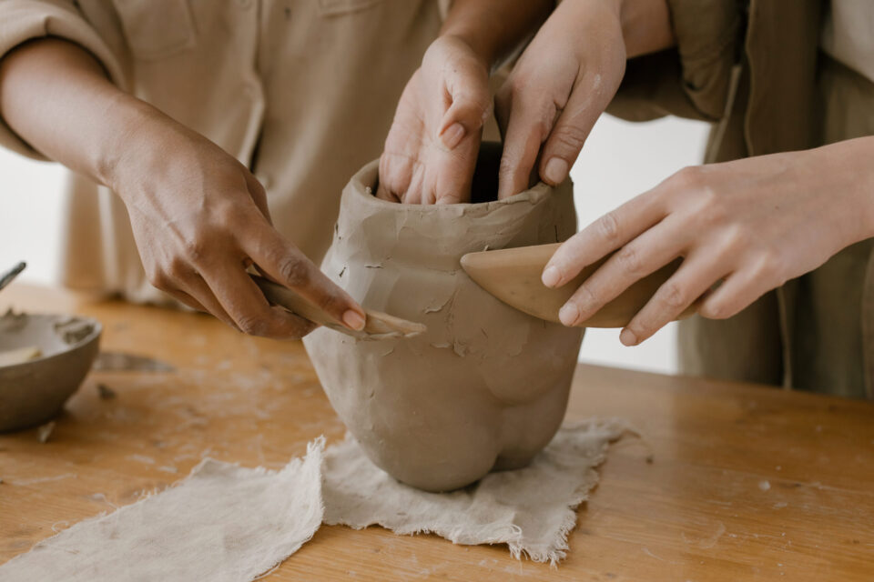 Shaping clay pots with hands and wood knife