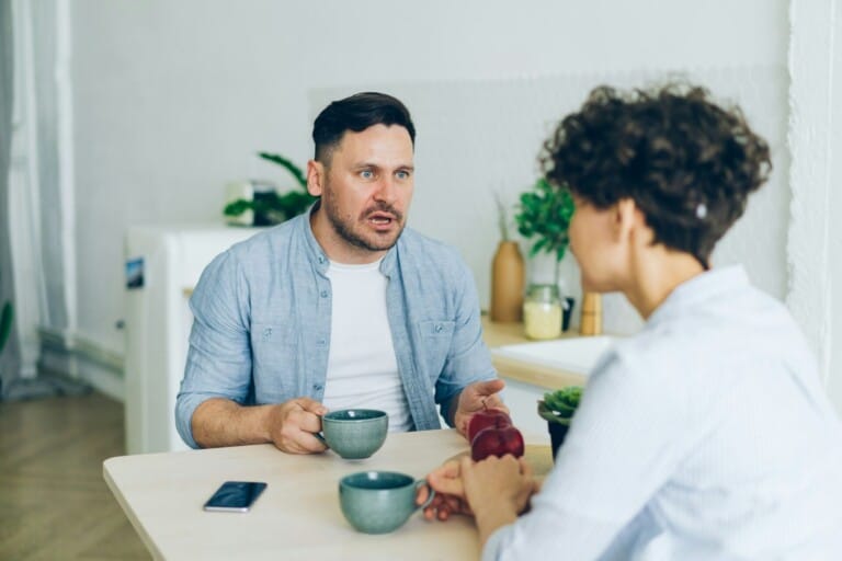 Unhappy couple man and woman agruing sitting at table in kitchen talking