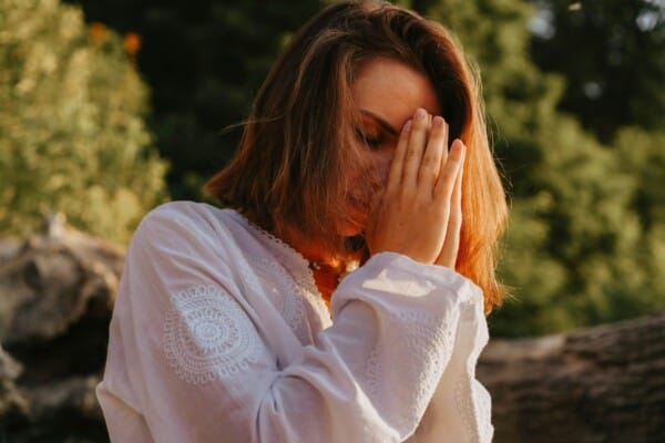 Woman in white long sleeves praying outside