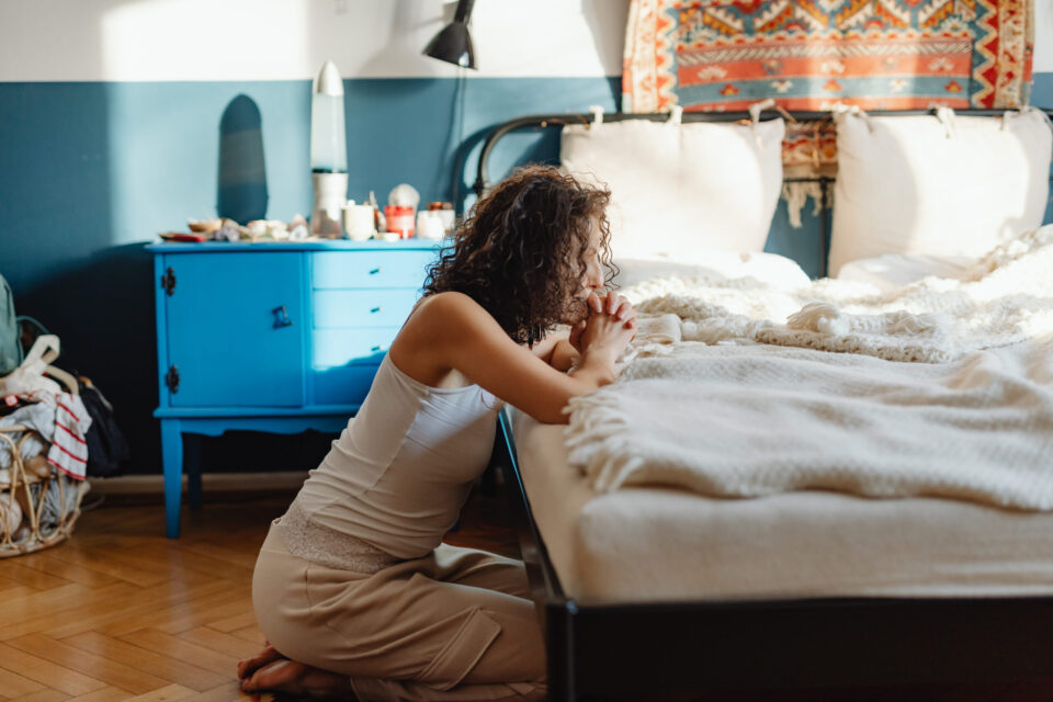 Woman in white tank top praying on a bed