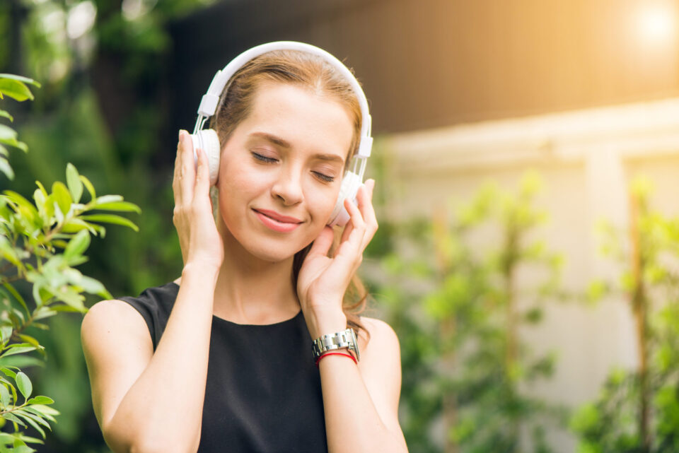 Woman wearing black sleeveless dress holding white headphone at daytime