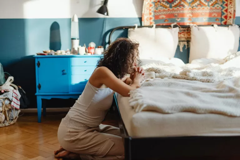 Woman in white tank top praying on a bed